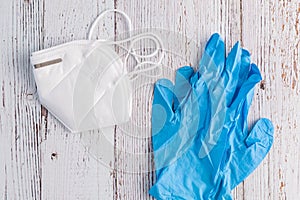 White commercial KN95 protective face mask and blue nitrile gloves on a white rustic background
