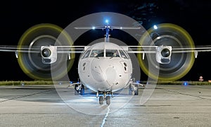 White commercial plane with engines running and propeller blur on a night with the moon on background