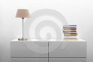 White commode with lamp and books in bright interior photo