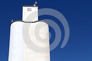 White community co-op cooperative agricultural farm feed grain and corn silo building against a blue sky in rural heartland