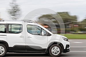 A white compact van is driving down the street. Fast delivery of cargo and small packages. Motion blur