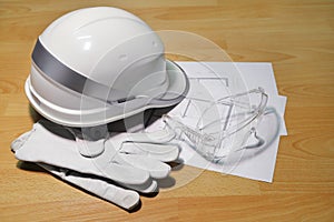 White construction helmet, safety goggles and leather gloves on project drawing