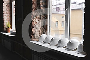 White construction helmets lie on the windowsill in a row inside the building under construction.