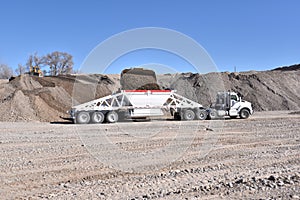 White construction truck and trailer being loaded with gravel with loader in gravel pit