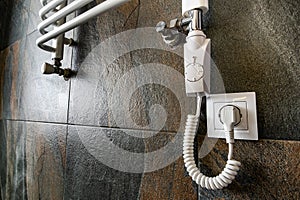 White contemporary electric towel dryer mounted on black tiled wall in modern bathroom