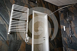 White contemporary electric towel dryer mounted on black tiled wall in modern bathroom