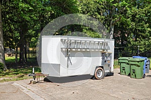 White contractor\'s supply trailer with attached ladder in a driveway near trash cans