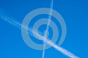 White contrails like X of two planes in clear blue sky. Jet trails on blue sky.