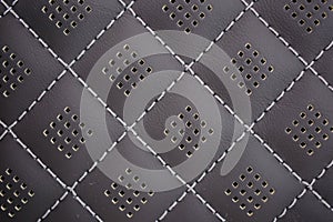 White contrast thread on perforated natural black leather car seat close-up