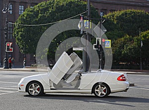 A white convertible with open doors stands on a city street