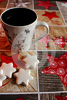 White cookies stars and cup decorated with elks on festive tablecloth with stars and wooden pattern.