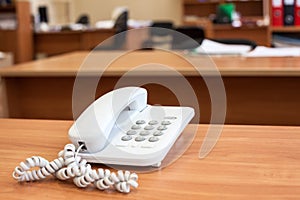 White corded telephone standing on office desk, empty room