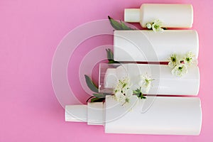 White cosmetic bottles, soap, massage brush, sponge, with cherry flowers on pink background. Natural cosmetics concept