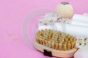 White cosmetic bottles, soap, massage brush, sponge, with cherry flowers on pink background. Natural cosmetics concept