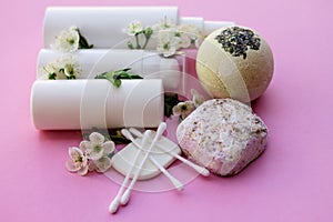 White cosmetic bottles, soap, massage brush, sponge, with cherry flowers on pink background. Natural cosmetics concept