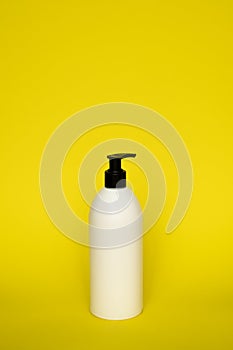 White cosmetic plastic bottle with black pump dispenser on yellow background. Liquid container for gel, lotion, cream