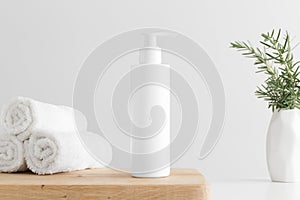 White cosmetic shampoo dispenser bottle mockup with towels and a rosemary  on a wooden table