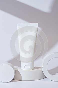 white cosmetic tube on a white background on white concrete podium. The concept of a cream with natural ingredient and