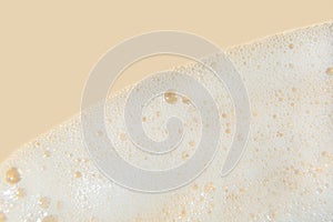 White cosmetics foam texture on beige background. Cleanser, shampoo bubbles, wash - liquid soap, shower gel, shampoo