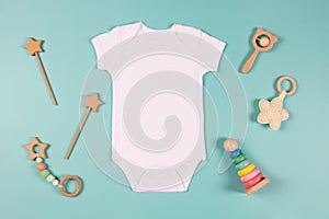 White cotton baby short sleeve bodysuit and natural wooden toy on light blue background. Infant onesie mockup. Blank