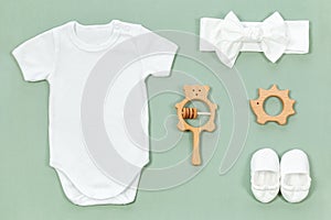 White cotton bodysuit for baby mockup in eco style on a mint green background. Cute booties, headband, wooden rattle and teethers