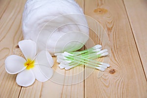 White cotton bud with cotton roll and white flower over wooden t