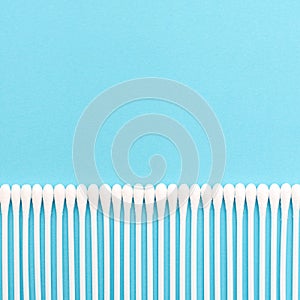White cotton buds on a blue background lie in a straight line at the bottom of the photo
