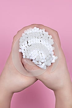 White cotton ear buds in the hands of a woman on a pink background