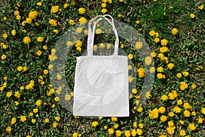 White cotton or mesh bag on dandelion green grass background. Zero waste, no plastic eco friendly shopping, recycling