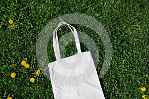 White cotton or mesh bag on dandelion green grass background. Zero waste, no plastic eco friendly shopping, recycling