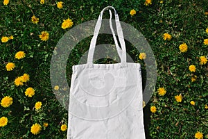 White cotton or mesh bag on dandelion green grass background. Zero waste, no plastic eco friendly shopping, recycling