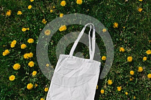 White cotton or mesh bag on dandelion green grass background. Zero waste, no plastic eco friendly shopping, recycling