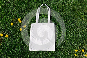 White cotton or mesh bag on dandelion green grass background. Zero waste, no plastic eco friendly shopping, recycling