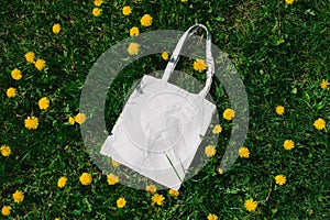 White cotton or mesh bag on dandelion green grass background. Zero waste, no plastic eco friendly shopping, recycling