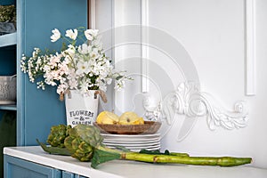 White countertop with flowers, branch of artichoke and vegetables on wooden plates