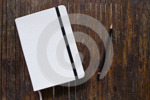 White cover notebook with black pencil on rustic wooden table flat lay photo.