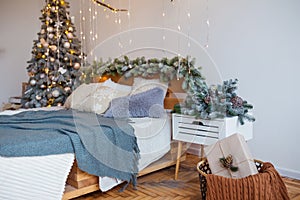 White cozy modern bedroom with holiday decoration. Wooden bed in scandinavian style room with festive Christmas tree in