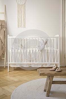 White cradle and shoes on wooden stool in baby`s bedroom interior with round rug