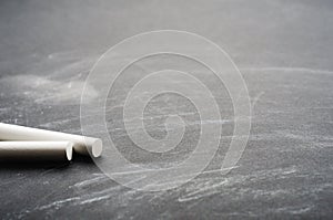 White crayons on a painted black board. School board, conceptual background. Copy space, close-up.