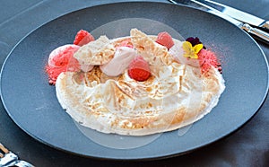 White cream desert with raspberries on black plate in restaurant.