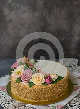 White cream honey cake decorated with buttercream flowers peonies, roses, chrysanthemums, scabiosa on gray background with lace