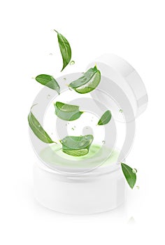 White cream jar with flying aloe vera slices and green leaves, isolated on white background.