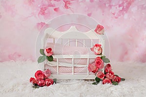 A white crib for a newborn baby adorned with pink rosebuds stands on a floral pink background