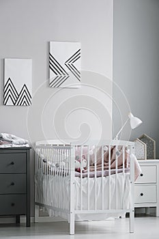 White crib with paste pink bedding and cotton balls in bright bedroom interior