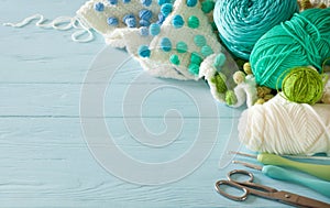 White crocheted fabric with color patterns. Bright aquamarine, blue and green yarn. Crochet hooks