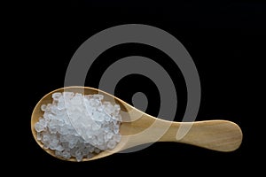 White crystals sea salt on wooden spoon on black background