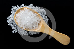 White crystals sea salt on wooden spoon on black background