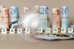 Cubes spelling Save Money on the table with an illuminated light bulb and Dinero bills photo