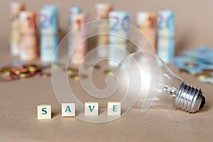 Cubes spelling Save Money on the table with an illuminated light bulb and Dinero bills photo