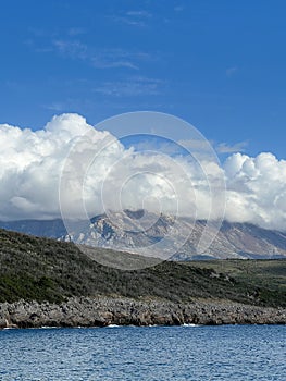 White cumulus clouds descend on a green mountain range by the sea